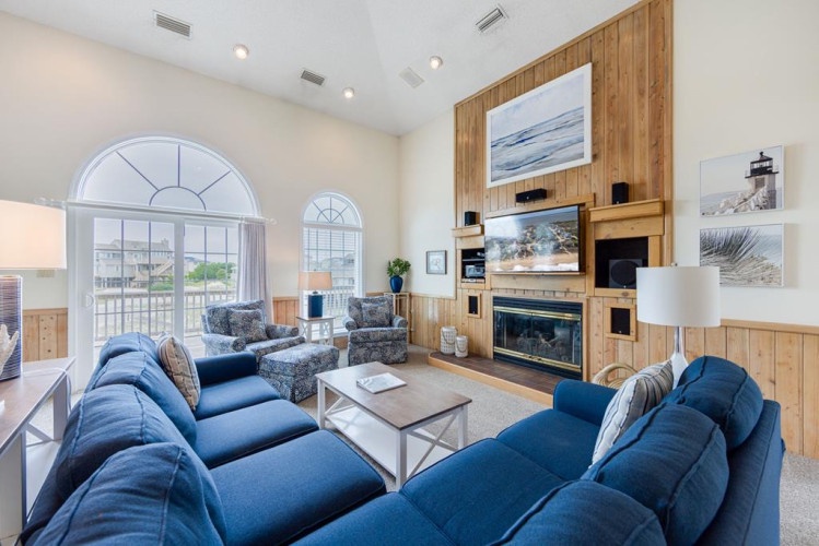 Your spacious living room welcomes you with comfortable sofas, a cozy fireplace, and coastal artwork that brings the beach indoors. Relax by the fireplace or enjoy views through the arched windows.