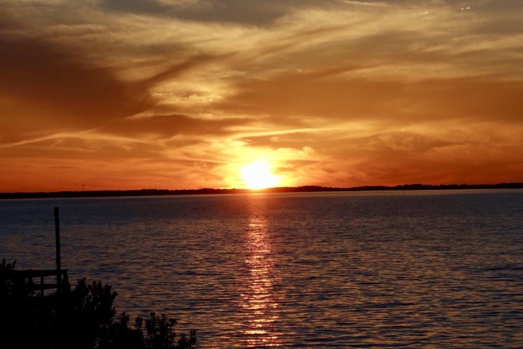 A breathtaking sunset paints golden hues across calm waters, showcasing the stunning natural beauty surrounding the property—an idyllic waterfront location for peaceful getaways.