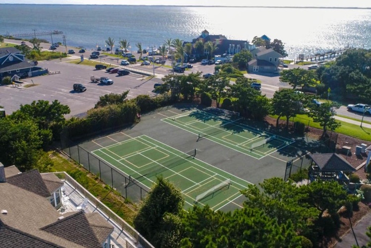 Aerial view captures tennis courts, parking, and waterfront access within a well-maintained resort community on sunny coastal grounds.
