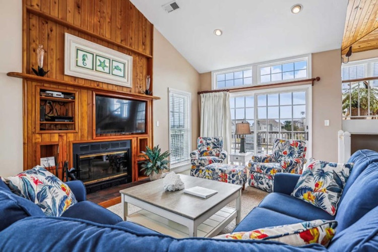 Sink into vibrant seating by a warm fireplace, with vaulted ceilings and expansive windows framing peaceful neighborhood views that invite relaxation.