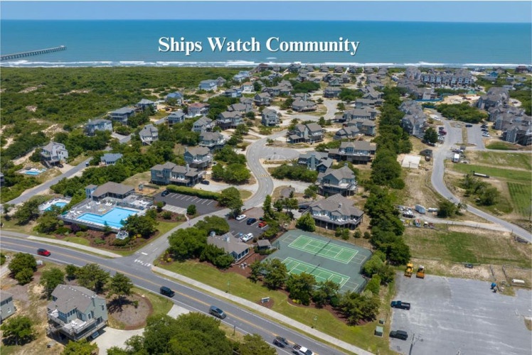 Aerial perspective of Ships Watch Community, a coastal residential neighborhood with tennis courts, a swimming pool, and natural dune landscapes near the oceanfront pier.