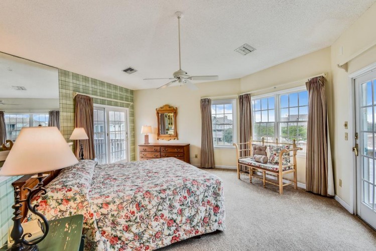 Your bright bedroom features a plush floral bed, classic wood furnishings, and French doors opening to your private balcony with scenic water views—perfect for morning coffee.