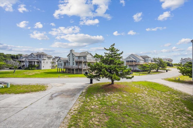 A quiet coastal neighborhood with spacious beach homes set along sandy lots and winding streets, framed by native pine trees and open sky.