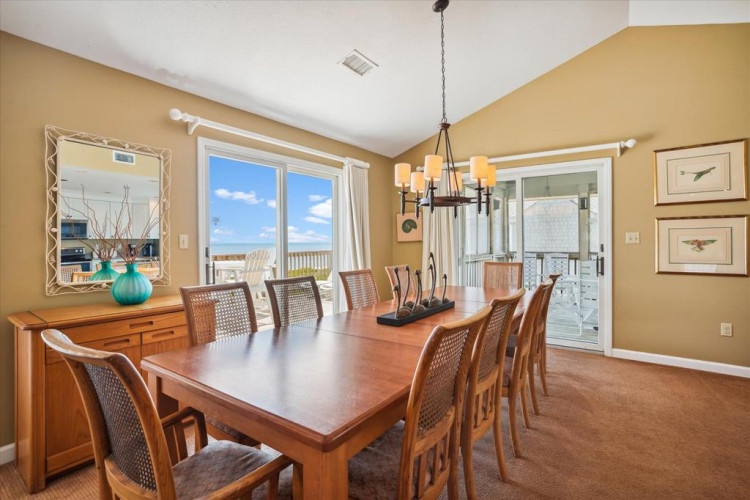 Gather around this spacious dining table where sunlight and ocean breezes pour through wide windows—perfect for long meals with loved ones and easy access to the deck.
