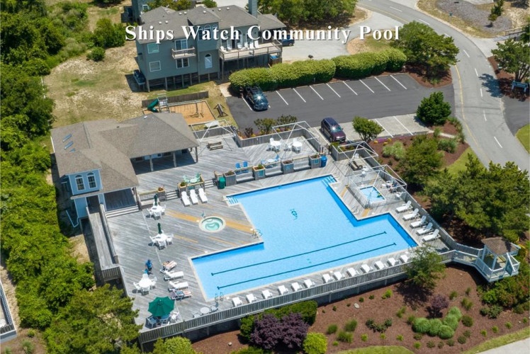 Aerial view of Ships Watch Community Pool featuring a large swimming pool with deck seating, surrounded by landscaped gardens, resident buildings, and dedicated parking area.