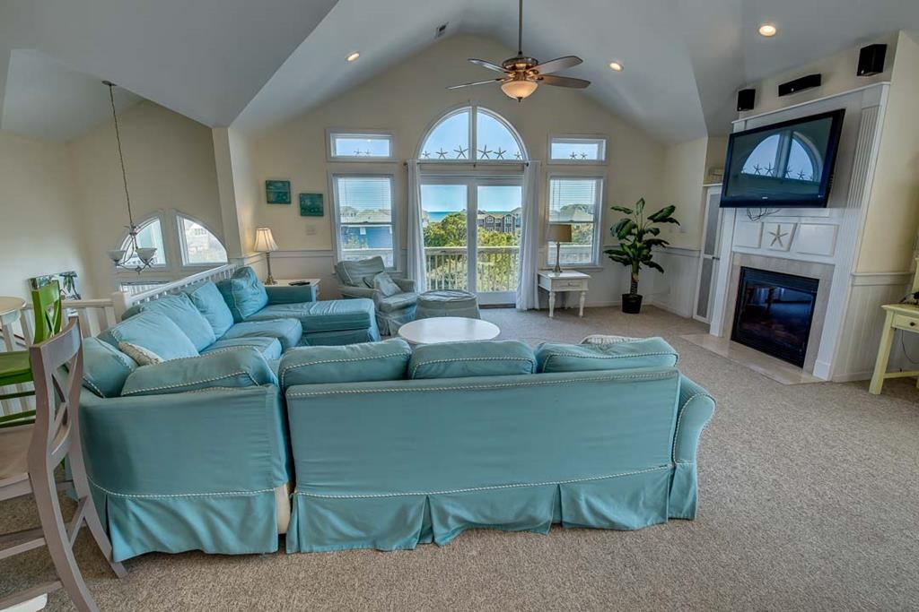 Unwind in your airy living room with vaulted ceilings, plush seating, and stunning coastal views through grand arched windows. The cozy fireplace and modern amenities ensure comfort after sun-soaked beach days.
