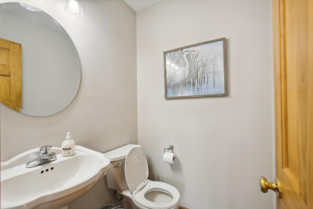 A clean, neutral-toned powder room offers simple comfort with a pedestal sink, soft lighting, and tasteful artwork to refresh during your stay.