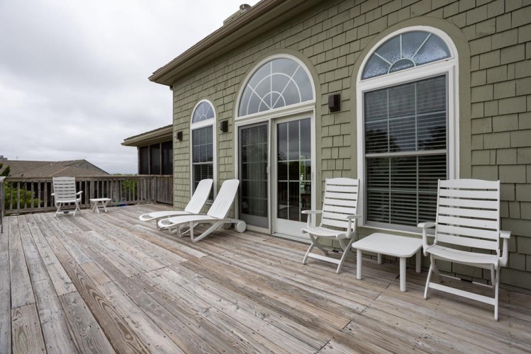 Your private deck awaits with lounge chairs and Adirondack seating, framed by elegant arched windows that fill the space with natural light and coastal charm.