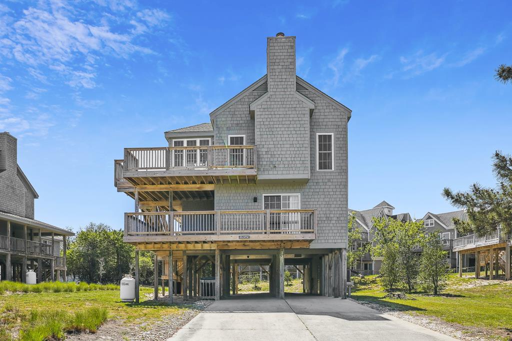 Elevated coastal property featuring multiple balconies and covered parking, set in a lush residential neighborhood with surrounding green spaces.