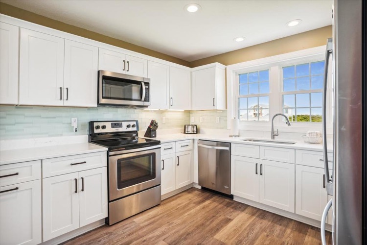 Step into this bright, spacious kitchen with gleaming stainless steel appliances, crisp white cabinetry, and warm wood-look floors. Large windows flood the space with natural light, making meal prep a pleasure.