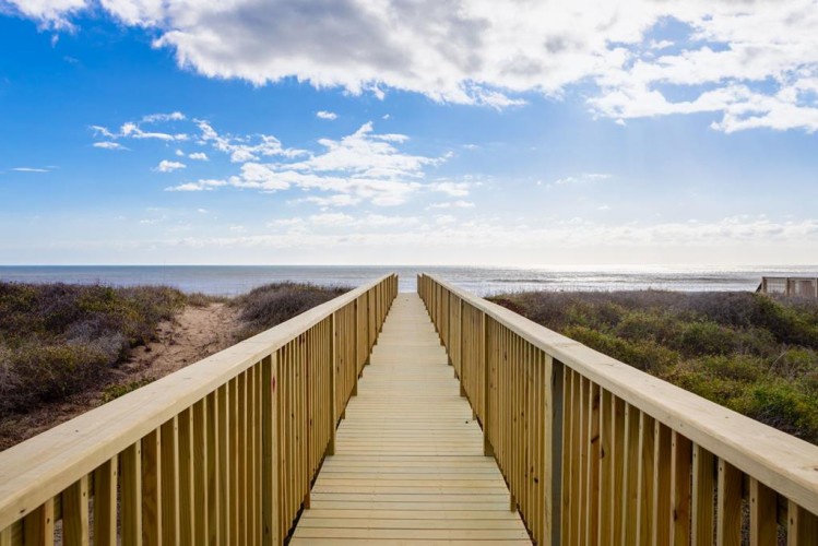 A wooden boardwalk leads through coastal dunes toward the beach and ocean, offering direct access to the shoreline and scenic views of the surrounding natural landscape.