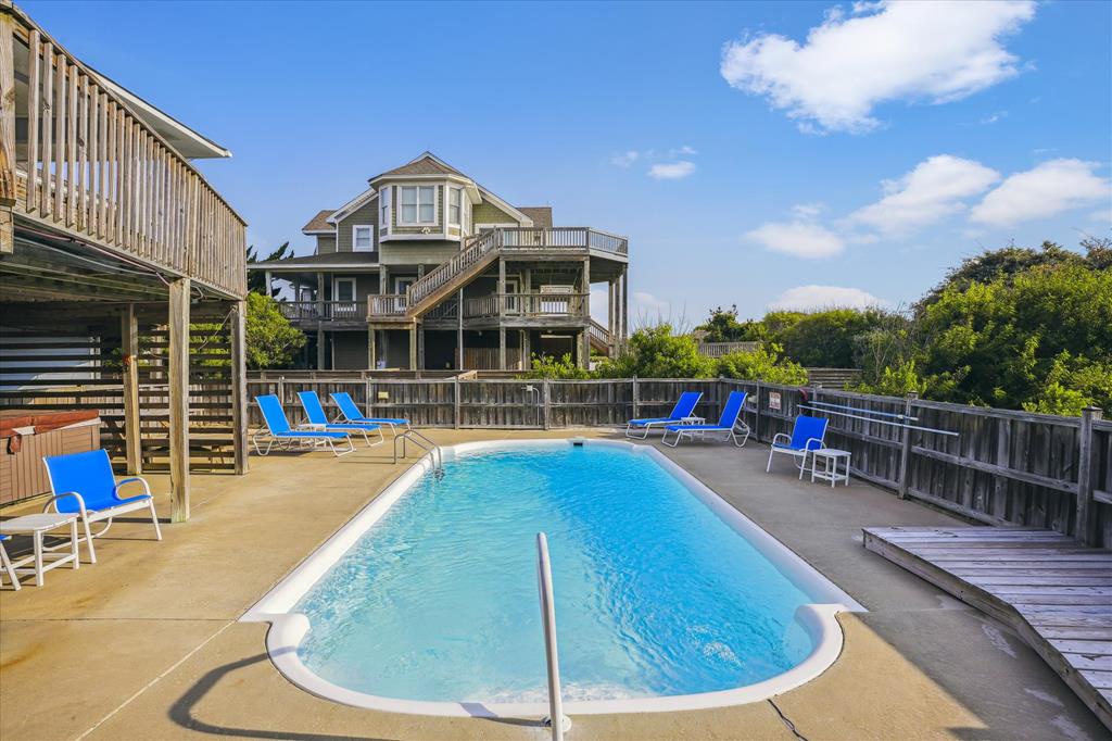 This elevated beach house offers pool access and multiple deck levels. Relax on the blue lounge chairs around the private pool, surrounded by coastal greenery and sunny skies.