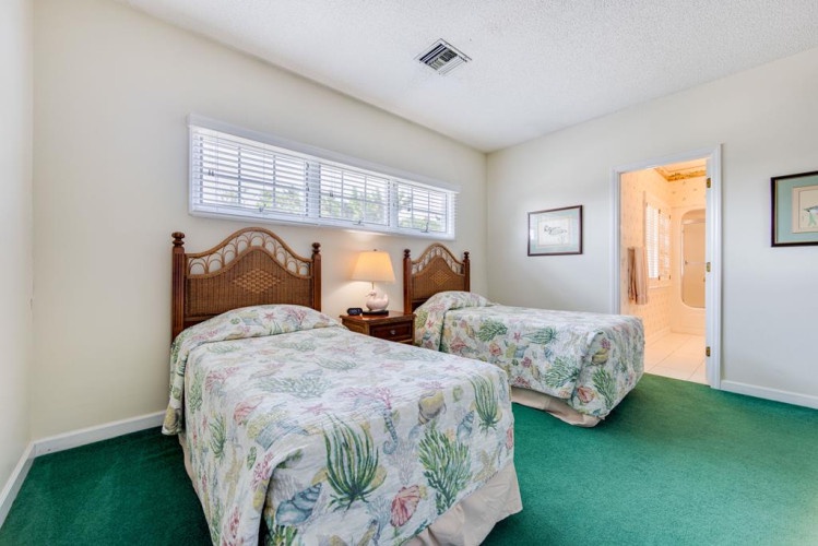 Your cozy guest bedroom features two comfortable twin beds with tropical bedding, warm lighting, and bright natural light from the large window—perfect for friends or family.