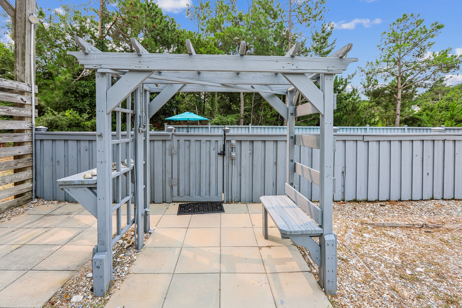 A charming outdoor shower awaits, framed by a weathered pergola and surrounded by lush greenery. Rinse off in the fresh air after a day at the beach, enjoying the peaceful, private setting.