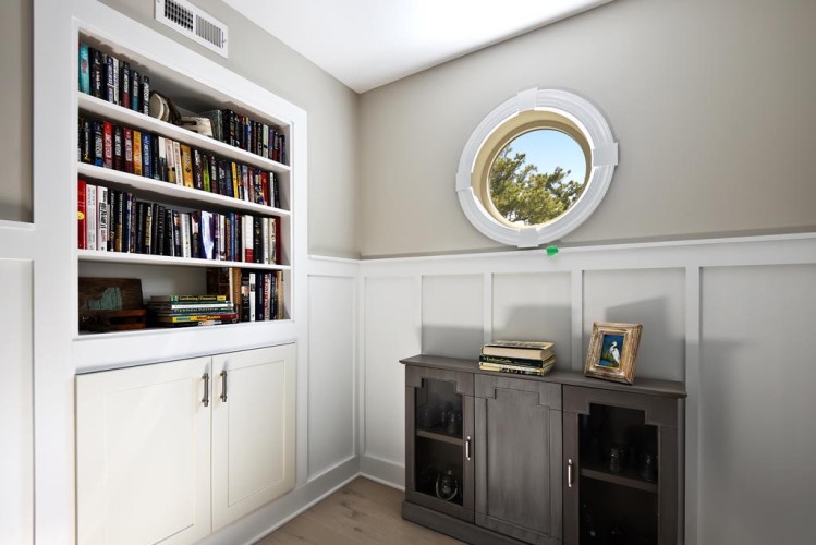 Step into your cozy reading nook where floor-to-ceiling shelves filled with books await your next adventure, while natural light spills through a charming porthole window.