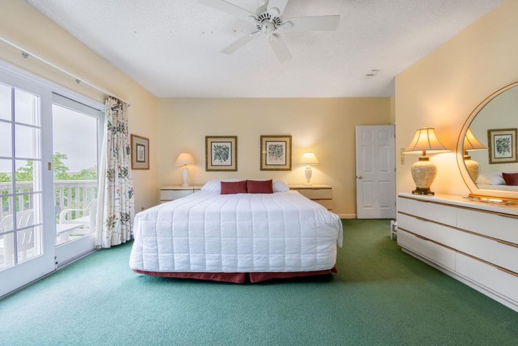 Unwind in your spacious bedroom featuring a plush bed, natural light from balcony doors, ceiling fan, and thoughtful furnishings for your comfort.