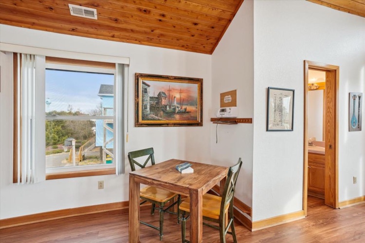 Enjoy meals at your cozy dining table beneath the warm wood ceiling, with coastal views through the window inviting natural light into your retreat.