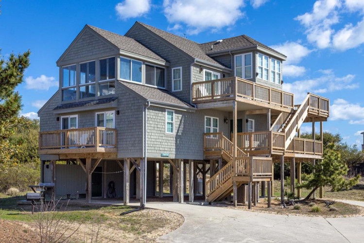 A classic coastal beach house elevated on stilts, featuring multiple levels of wooden decks and balconies overlooking the natural landscape, offering a perfect seaside retreat.