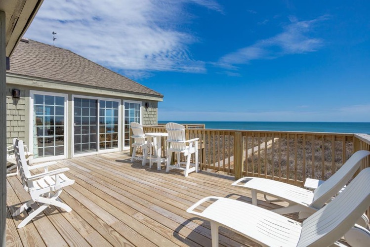 Picture yourself here on this spacious deck, soaking up ocean breezes and stunning sea views. Relax on lounge chairs under clear blue skies, just steps from your cozy rental.