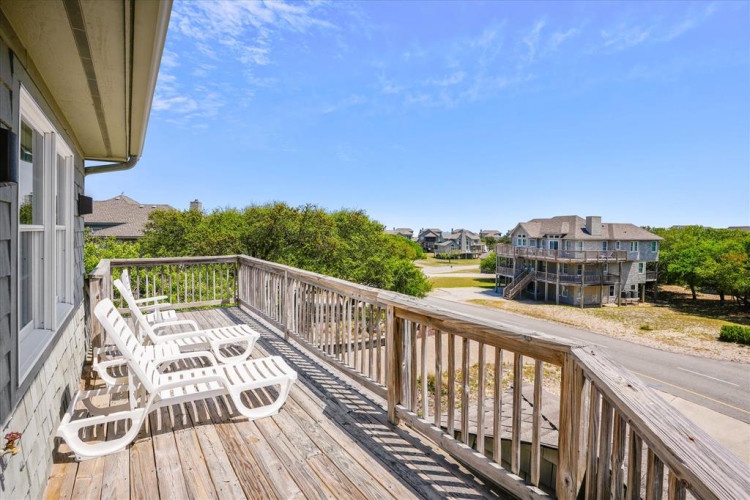 A spacious deck with lounge seating overlooks a coastal neighborhood with nearby homes and natural surroundings, offering a peaceful elevated setting.