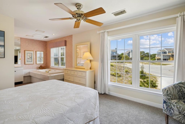 Wake up to sunshine streaming through large windows framing views of the coastal landscape. Your private sanctuary features a plush bed, ceiling fan, and an inviting en-suite with soaking tub—all designed for ultimate relaxation.