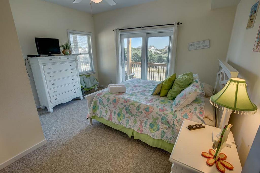 Sink into comfortable coastal vibes in your bright bedroom with sea turtle accents, a flat-screen TV, and balcony doors opening to soothing water views—your serene vacation retreat.