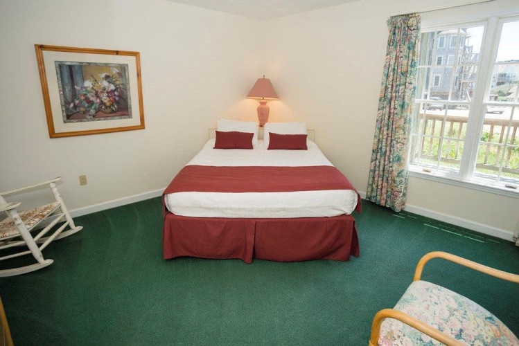 Your cozy bedroom awaits with a plush bed dressed in burgundy accents, cheerful floral curtains, and bright windows framing neighborhood views—perfect for a restful retreat.