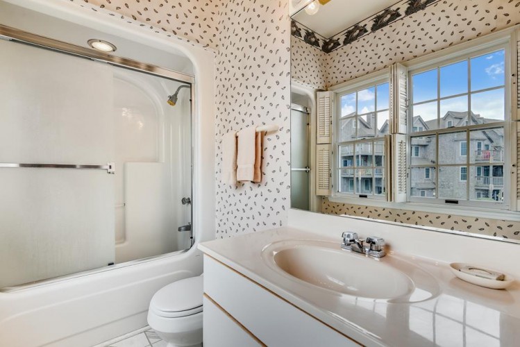 Step into your private bathroom, where natural light pours through large windows, illuminating clean white surfaces and vintage-inspired wallpaper that adds character to your morning routine.
