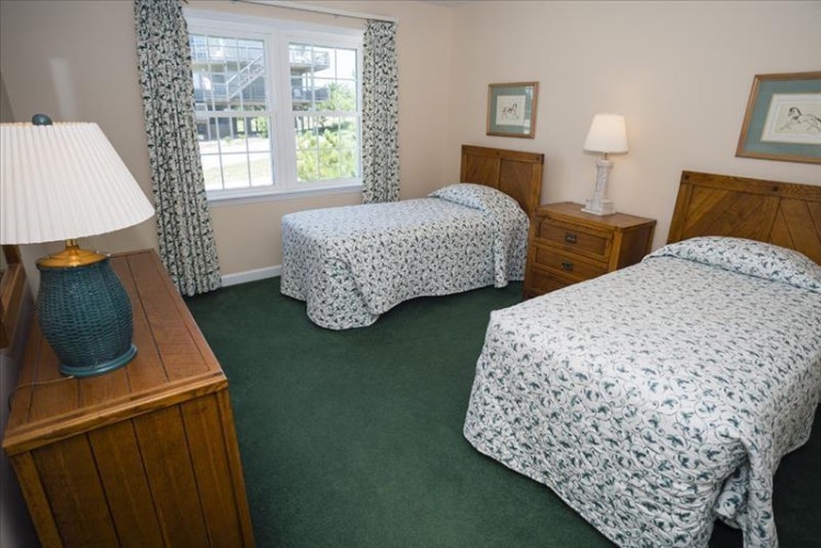 Relax in your comfortable twin bedroom, featuring matching floral bedding, warm wooden furnishings, and soft natural light from the large window overlooking the property grounds.