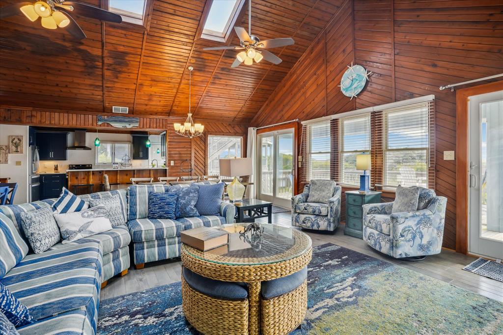 Relax in your spacious open-concept living area with vaulted wood ceilings, skylights, coastal décor, and sweeping views of the surrounding natural landscape. Perfect for unwinding together.