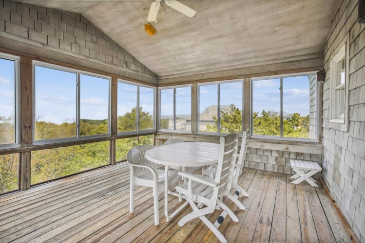 Enjoy your morning coffee at this sun-filled screened porch, where panoramic windows frame lush greenery and peaceful natural views, creating the perfect spot to unwind and breathe in the fresh air.