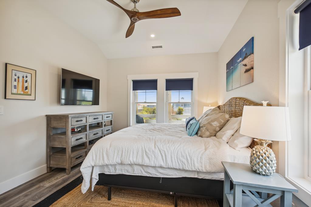Sink into plush bedding and unwind beneath the vaulted ceiling and gentle fan breeze. Wake up to serene views through the windows, with coastal artwork adding a tranquil touch to your retreat.