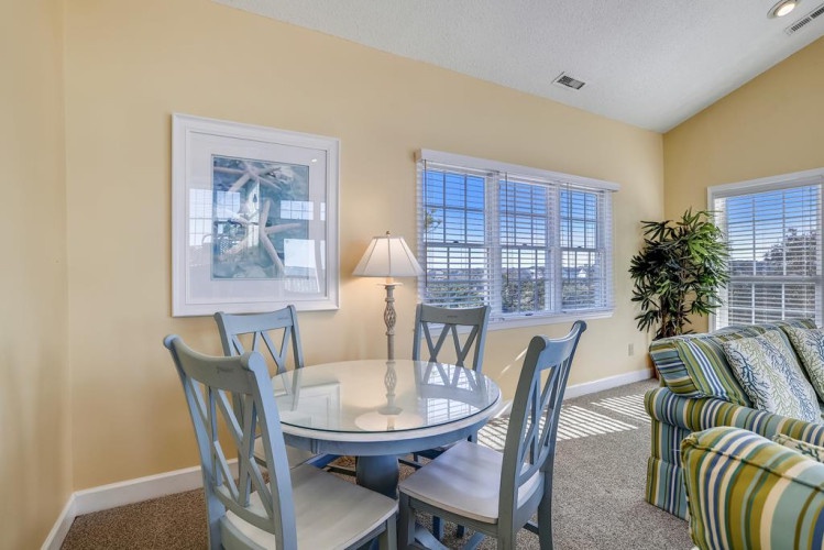 Picture yourself sharing meals at this charming glass-top table, sunlight streaming through white shutters as you plan your next adventure. The cozy striped seating invites you to linger over morning coffee or evening conversation.