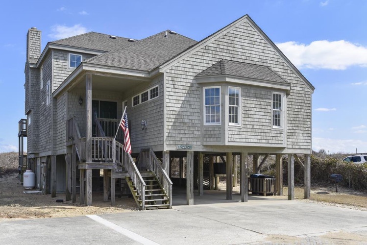 Elevated beachside property with classic shingled exterior, covered porch, and dedicated parking beneath the home—just steps from the shore.