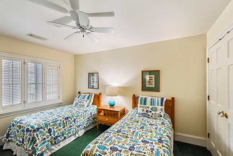 Two comfortable twin beds dressed in cheerful coastal linens await you in this bright and airy bedroom, complete with a ceiling fan, bedside table, and soft natural light.
