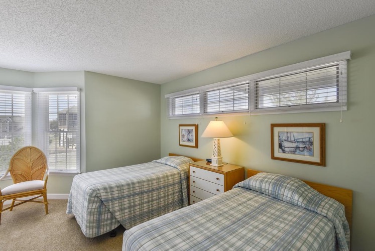 Your comfortable twin bedroom awaits with soft natural light, cozy plaid linens, and thoughtful touches like bedside lamps and coastal artwork to help you unwind after each day's adventures.