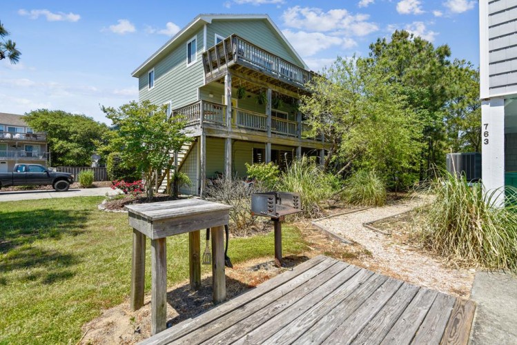 Three-story coastal home with multiple balconies and landscaped grounds, offering a welcoming arrival in a peaceful neighborhood setting.