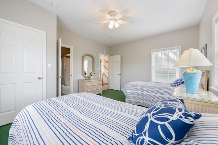 You'll rest easy in this bright bedroom with twin beds dressed in crisp blue-and-white linens. Natural light filters through the window, while a ceiling fan keeps the space comfortable.