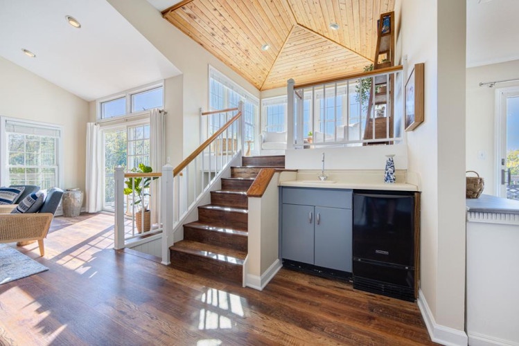 Sunlight streams through windows onto warm wood floors and a striking staircase leading to your private loft retreat, with thoughtful touches like a beverage station for easy mornings.