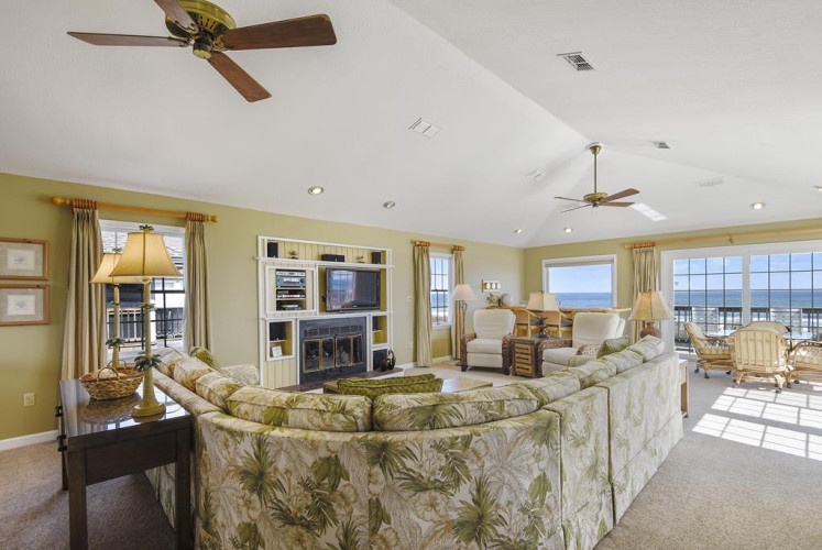 Relax in your bright, coastal living room with vaulted ceilings, ceiling fans, and stunning ocean views through expansive windows—your perfect retreat awaits.