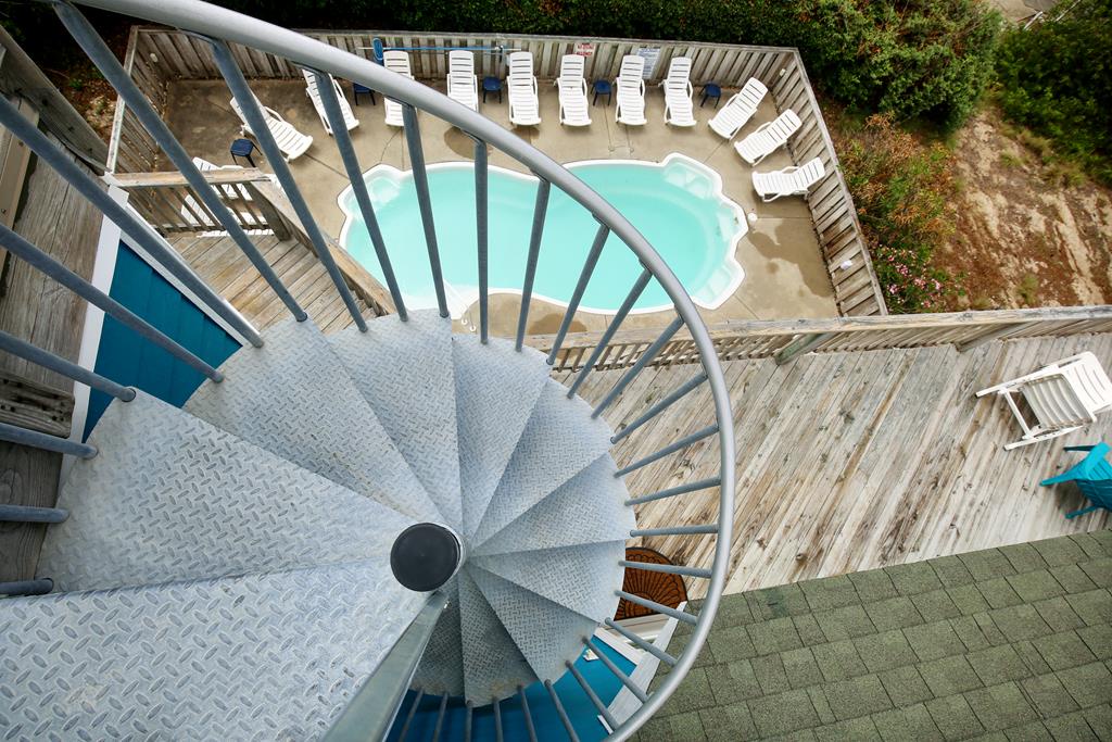 Elevated perspective showcasing the property's pool deck and surrounding natural landscape, with winding staircase descending from upper levels to pool area below.