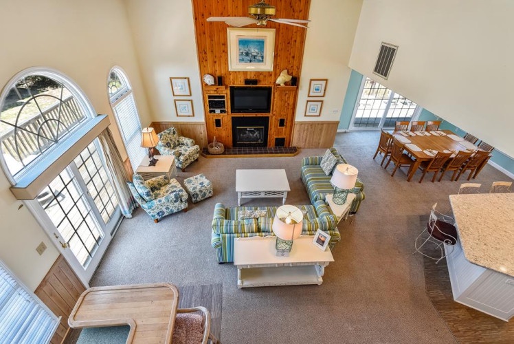 Settle into your open-concept living space where high vaulted ceilings and sunlit arched windows create an airy retreat. Gather by the cozy fireplace, share meals at the spacious dining table, or relax on coastal-inspired sofas—all designed for your comfo