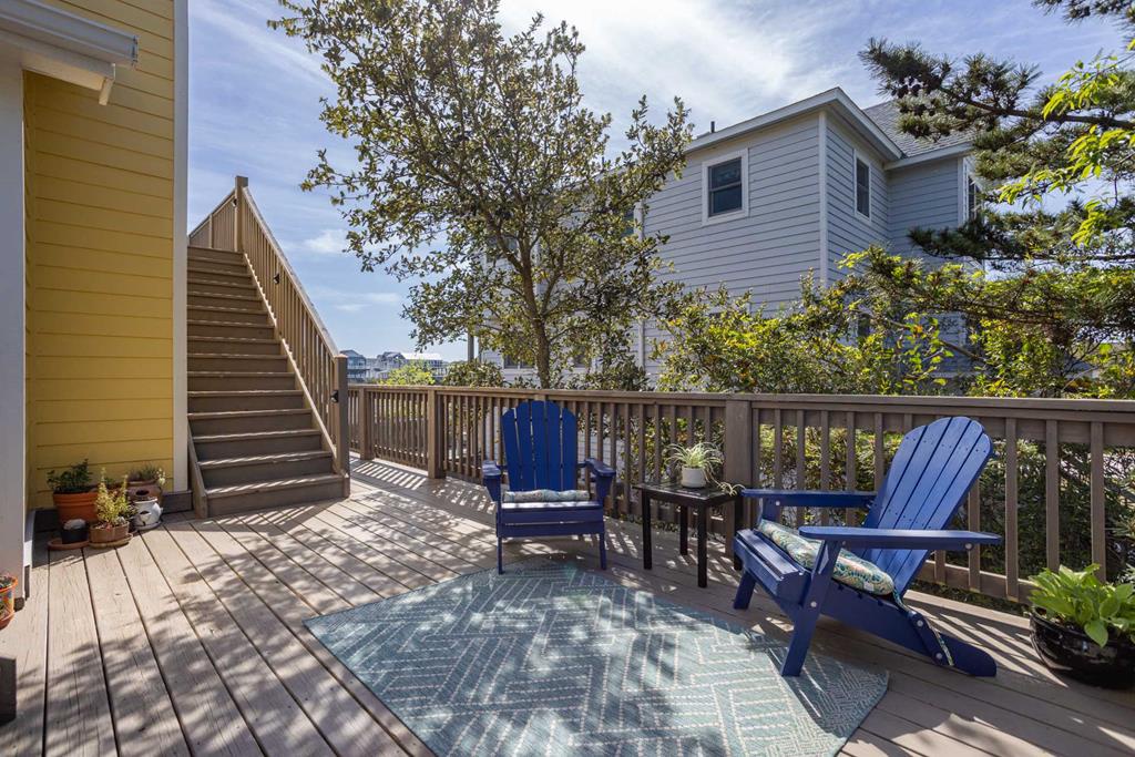 Relax in vibrant blue Adirondack chairs on your private deck, surrounded by leafy trees and coastal charm—a peaceful retreat for morning coffee or sunset unwinding.