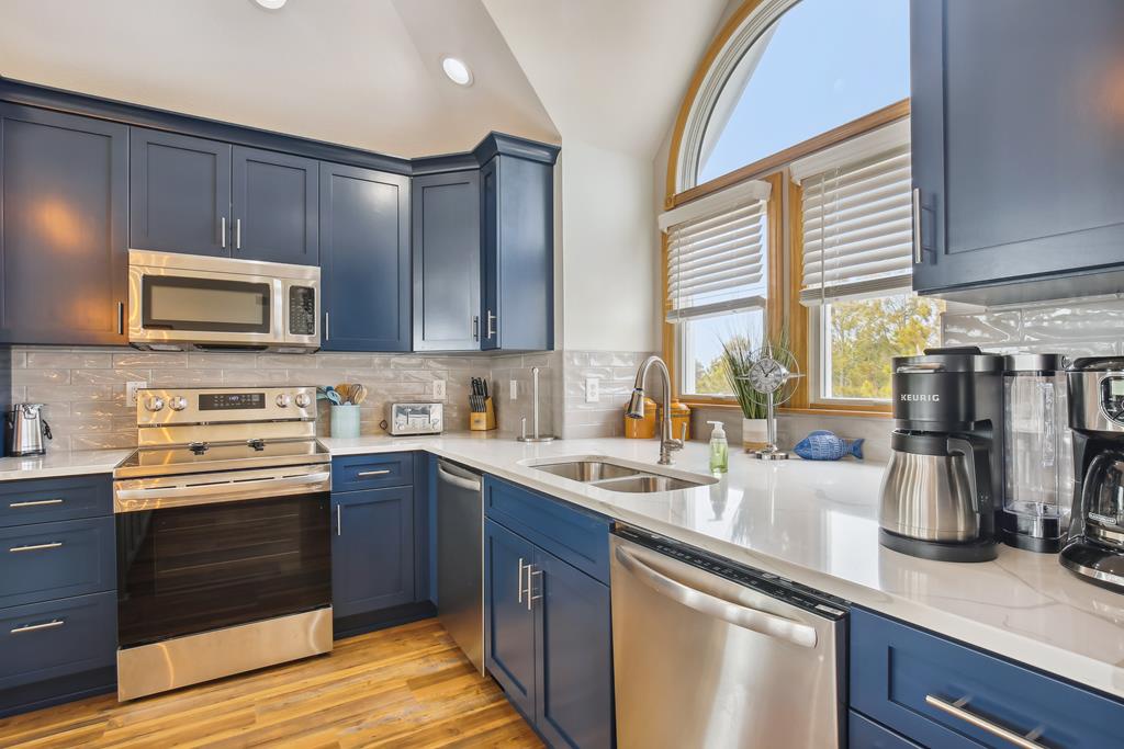 Your chef-inspired kitchen features sleek navy cabinetry, gleaming quartz countertops, and modern stainless appliances beneath a vaulted ceiling with charming arched windows. Every detail invites you to create memorable meals.