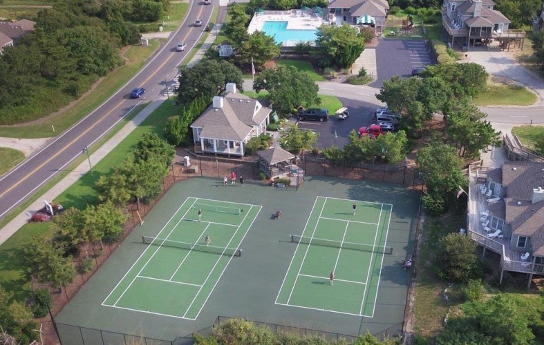 Aerial view reveals the property's tennis courts, swimming pool, and surrounding residential community accessible to guests during their stay.