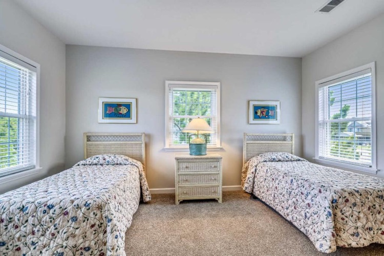 Your cheerful twin bedroom awaits with soft coastal linens, natural light from three windows, and charming seaside artwork that welcomes you to unwind after a day of adventure.