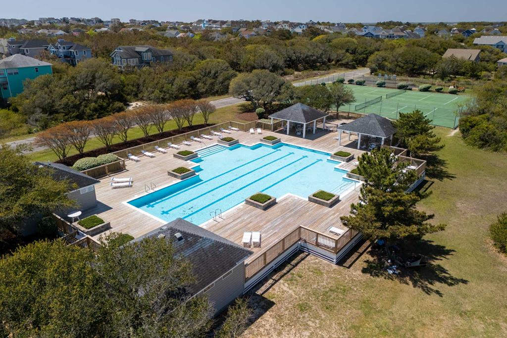 Aerial view of the community pool and recreational facilities surrounded by lush landscaping and coastal trees, with tennis courts and neighborhood homes nearby.