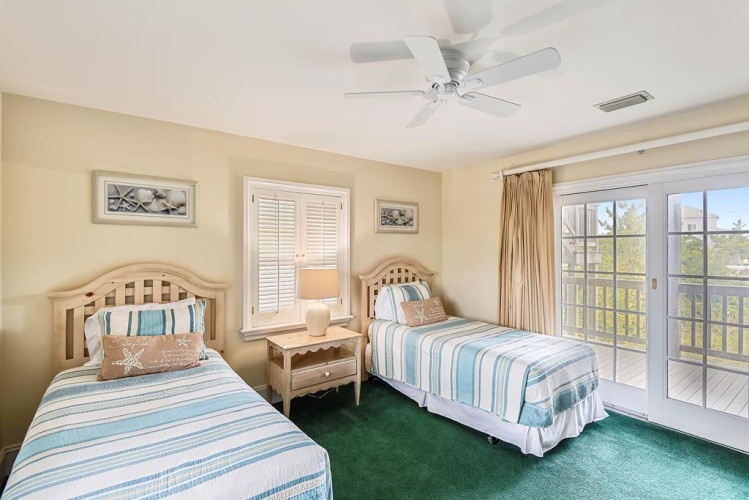 Your beach-inspired retreat awaits with two cozy beds dressed in coastal stripes, a private balcony framing sunny views, and a gentle ceiling fan keeping you cool and comfortable.