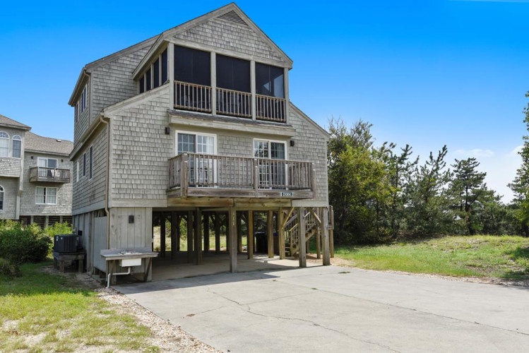 This distinctive coastal home features elevated construction and screened balconies, characteristic of beachside architecture. The property offers convenient parking and a driveway, with natural landscaping surrounding the entrance.