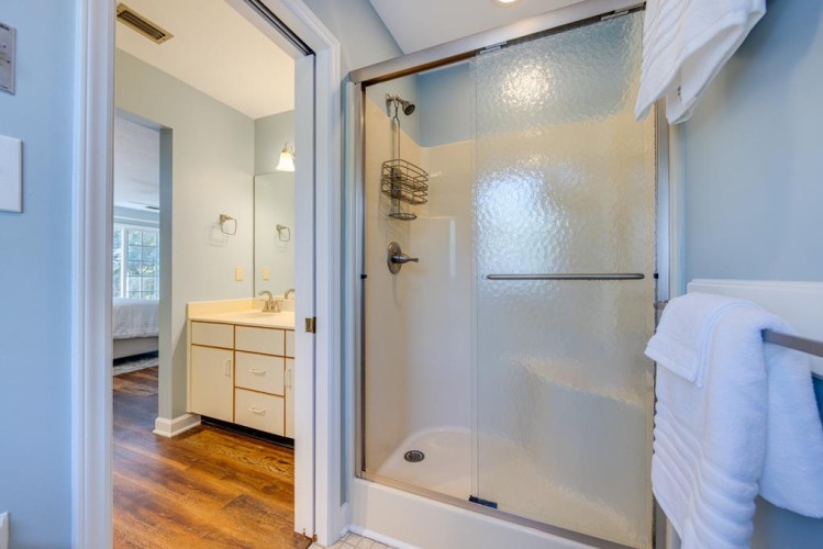Step into your private en-suite with a modern walk-in shower, fresh towels, and warm wood flooring that connects to the bedroom for ultimate comfort.
